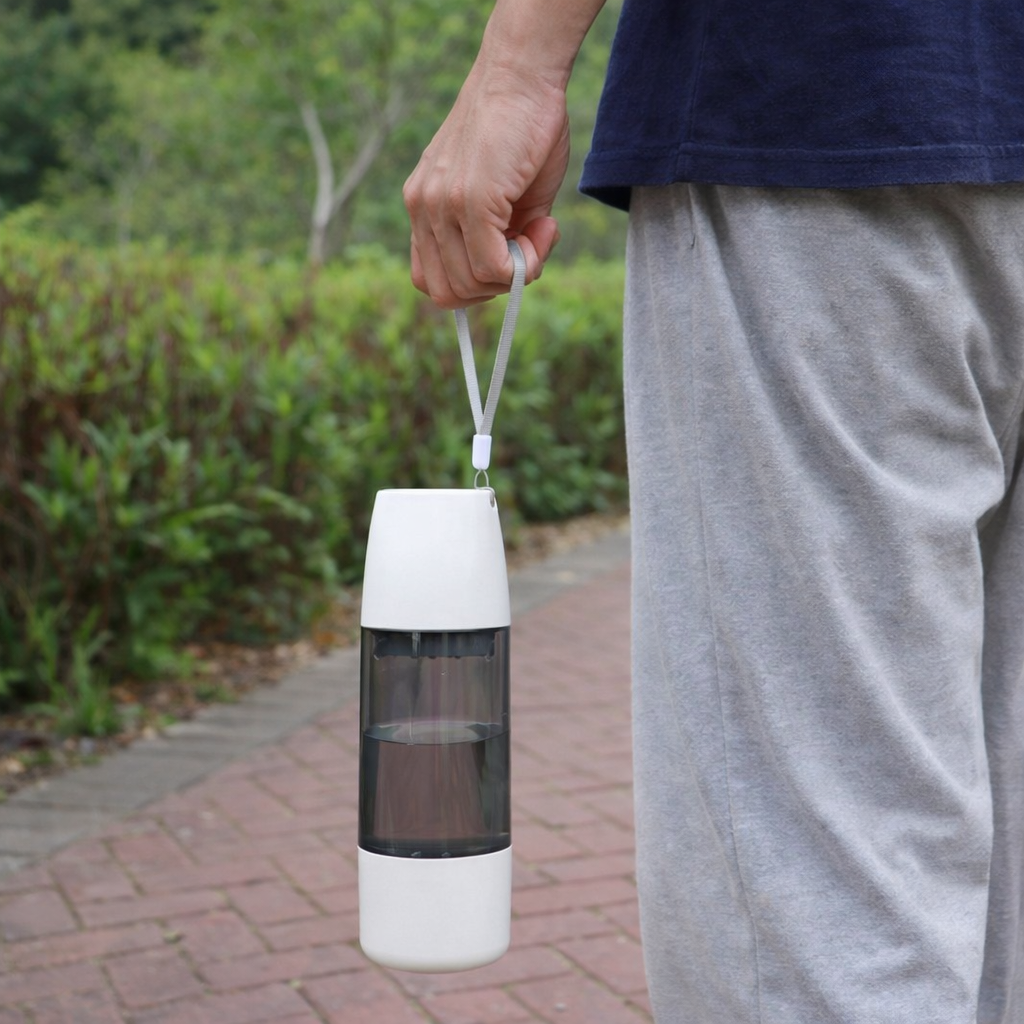 Person holding a white and black portable lantern outdoors on a path with greenery.
