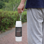 Person holding a white and black portable lantern outdoors on a path with greenery.