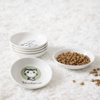 Set of white bowls with cat illustrations on a textured surface with cat food.