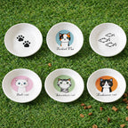 Set of six small white bowls with cat-themed illustrations on a grassy background